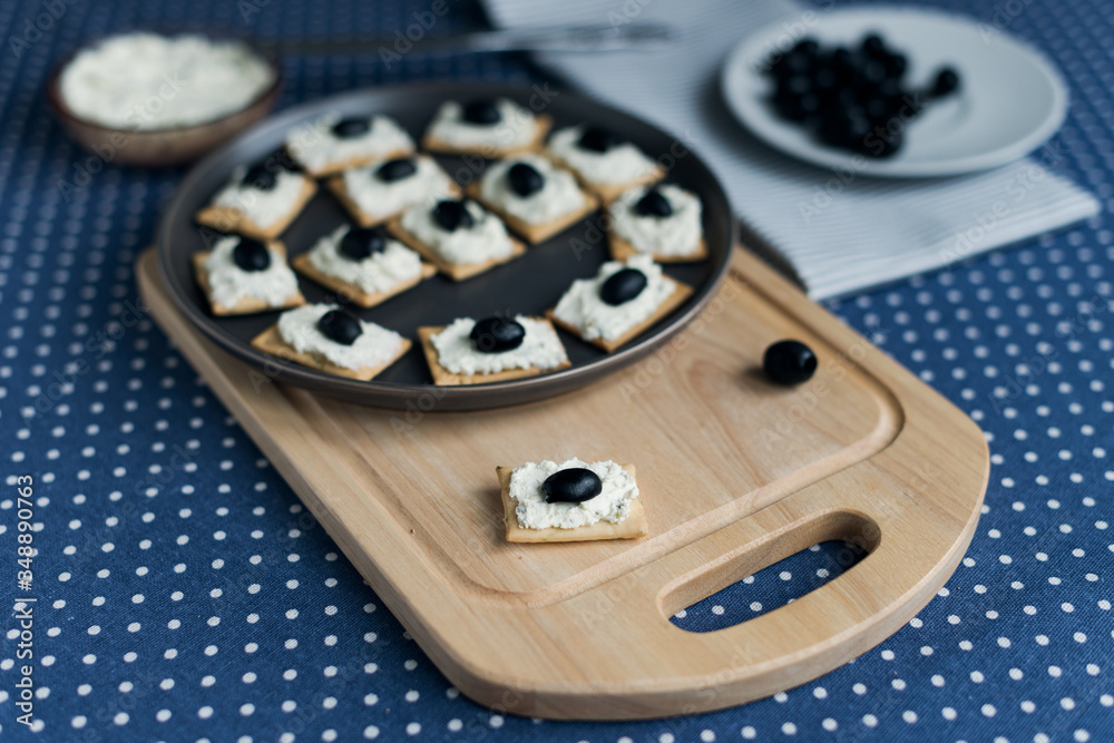 Plate with crackers with soft cheese and olives on a blue polka dot tablecloth. Plate with crackers with soft cheese and olives on a blue polka dot tablecloth.