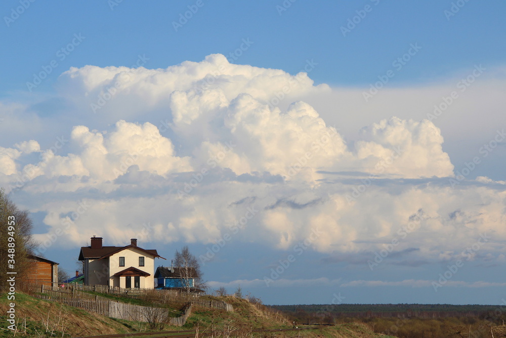Beautiful landscape with the horizon and with a white house on a hill. Countryside in spring with dry and young green grass. White cumulus clouds against the blue sky. Cottage on the edge of the