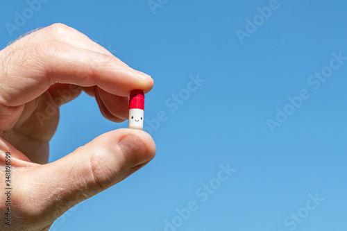 A man holding in his hand a funny smiling pill on the blue sky background. The cure for viruses, bacteria, allergies. Creative
