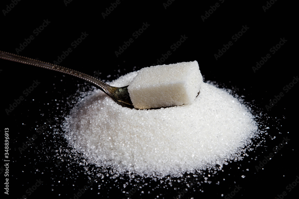 Sugar cube on a spoon. Spoon on a pile of sugar. Photo on a black background Sugar cube on a spoon. Spoon on a pile of sugar. Photo on a black background