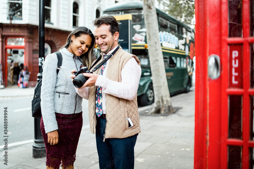 Fototapeta premium Happy travelling couple reviewing photos in London, UK. Double decker bus and red telephone booth in a frame.