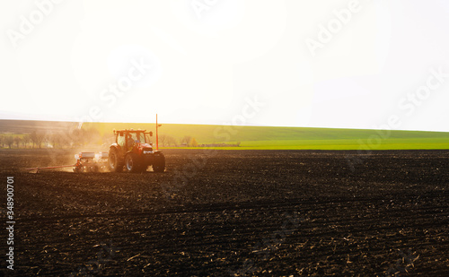 Farmer with tractor seeding sowing crops at agricultural fields in spring at sunset 