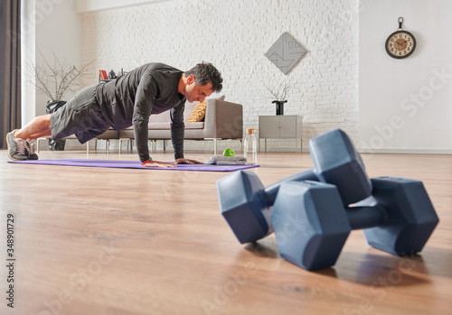 Strong sportive man doing exercises at home, close up dumbbell, sport mat, decorative background living room concept. © UnitedPhotoStudio