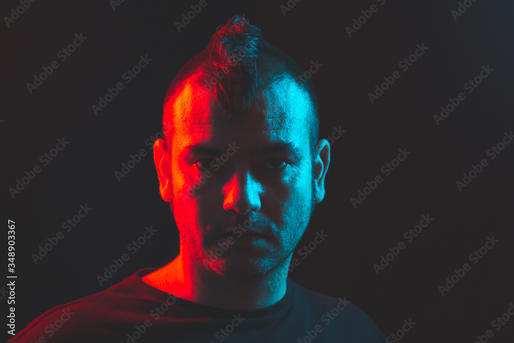 Caucasian man with a crest of hair, Illuminated with dramatic blue and red light looking seriously to the camera.