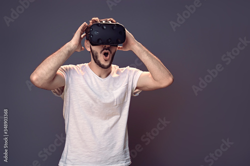 Technology, gaming, entertainment and people concept - Amazed happy smiling man with virtual reality headset or 3d glasses gesturing with his hand surprised in studio purple background copy space