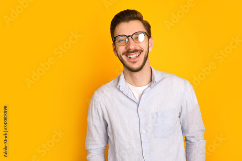 A young office worker with beard laughing out loud on yellow background, wearing a white shirt and glasses, looking at the camera, making jokes , feeling awesome, copy space © Pavel Shcherbakov