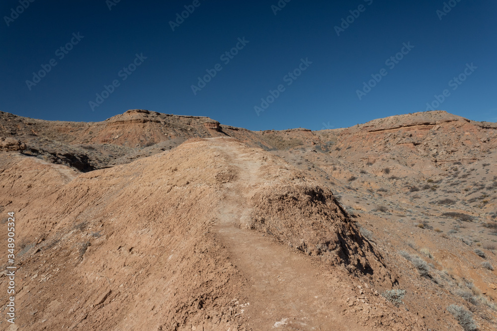 Hard packed mountain path along a ridge in the New Mexico desert, deep blue sky, road less traveled, horizontal aspect Hard packed mountain path along a ridge in the New Mexico desert, deep blue sky, road less traveled, horizontal aspect