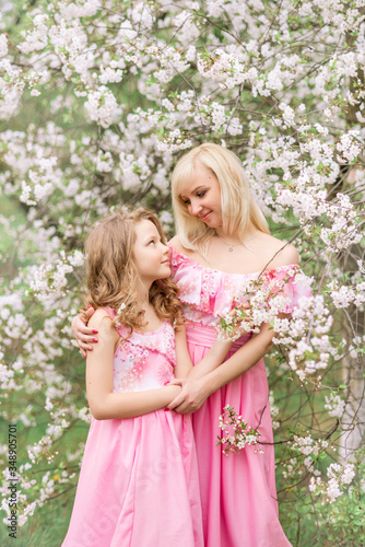 Mother and daughter in pink dresses in a blooming garden in spring.
