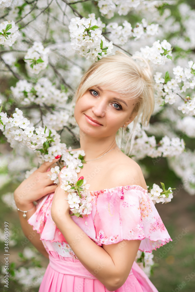 Fototapeta premium Portrait of a beautiful blonde woman in a pink dress in a blooming garden in spring.
