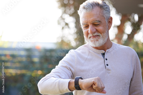 Senior Hispanic Man Checking Health Monitor On Smart Watch In Garden At Home photo