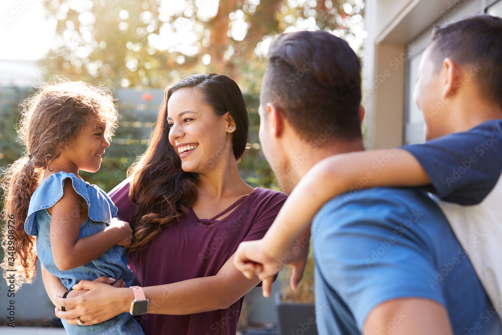 Smiling Hispanic Family With Parents Giving Children Piggyback Rides In Garden At Home Smiling Hispanic Family With Parents Giving Children Piggyback Rides In Garden At Home