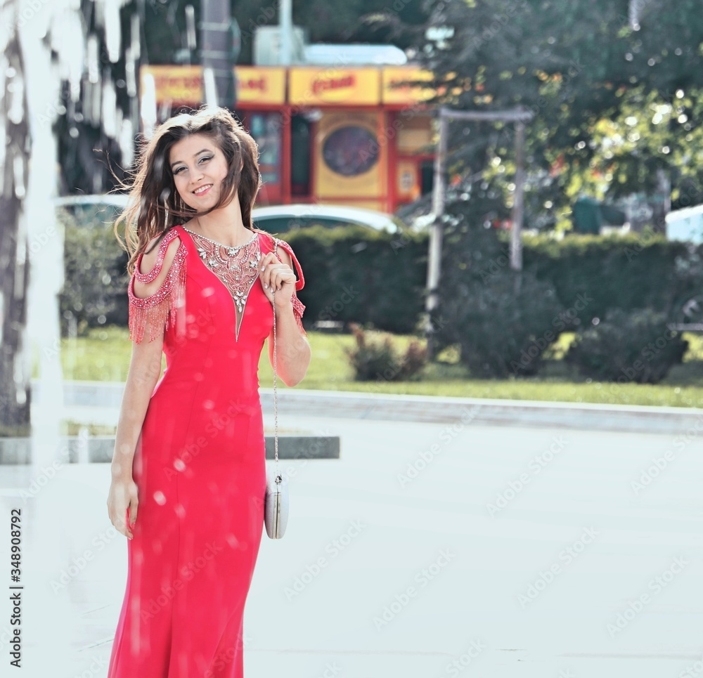 Fototapeta premium A beautiful young girl poses in an elegant red dress at her prom