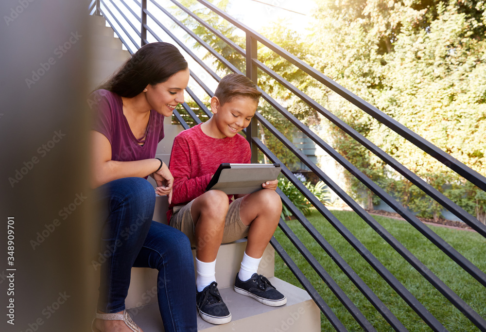 Mother Sitting On Steps Outdoors At Home With Son Using Digital Tablet