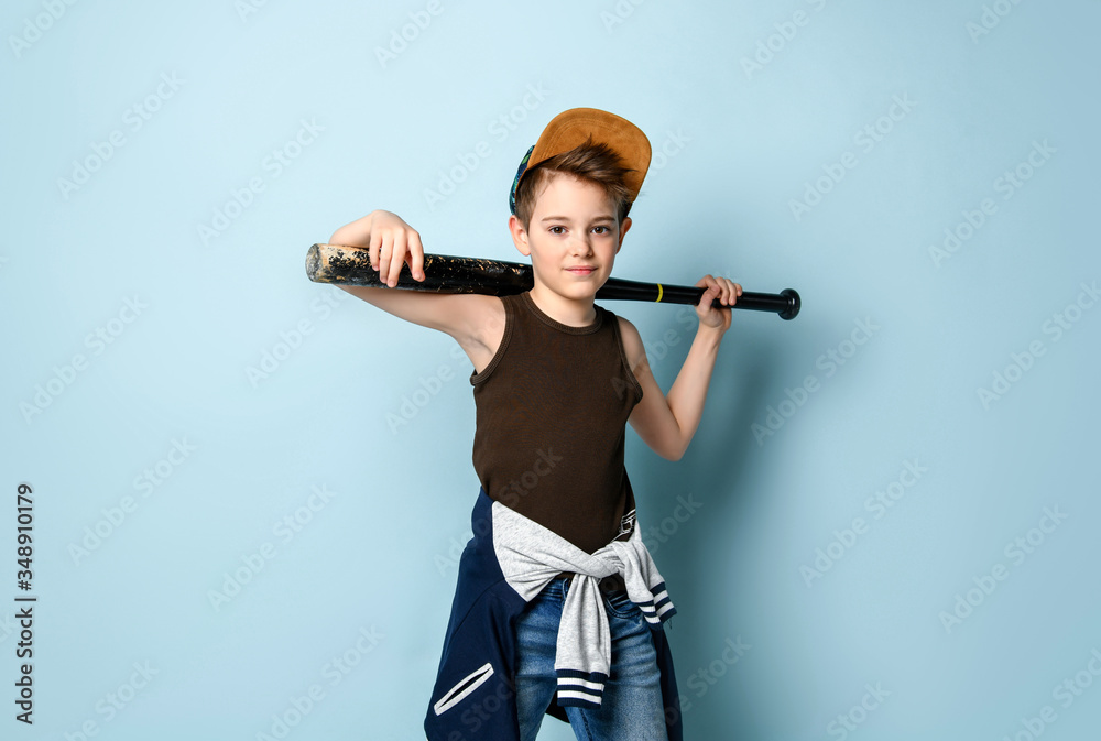 Naughty kid looking forward with a sly smile on face keeping baseball bat behind his head. Three quarter length portrait isolated on blue background Naughty kid looking forward with a sly smile on face keeping baseball bat behind his head. Three quarter length portrait isolated on blue background