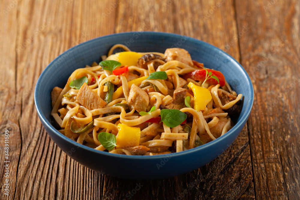 Fried chicken with mango and coconut milk with noodles. Prepared in a wok. Front view. Served in a blue bowl. Fried chicken with mango and coconut milk with noodles. Prepared in a wok. Front view. Served in a blue bowl.