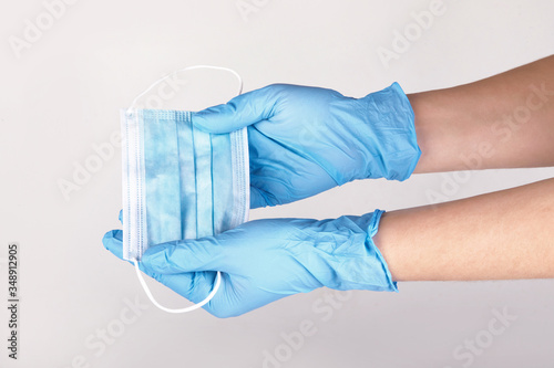 Hands in blue disposable medical gloves holding respiratory surgical facial mask on a grey background. Pandemic corona virus, insurance, airborne diseases, SARS, grippe. 