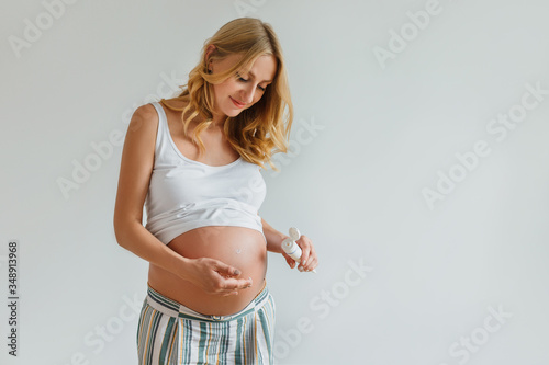 Pregnant blonde woman applying cream for belly to prevent stretch marks. Future mother holding in hands tube with lotion for skin care. Concept of health and body care, beauty during pregnancy