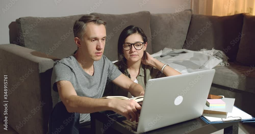 Young couple discussing a joint project or design of a new apartment working on a laptop at home in the evening. Young couple discussing a joint project or design of a new apartment working on a laptop at home in the evening.
