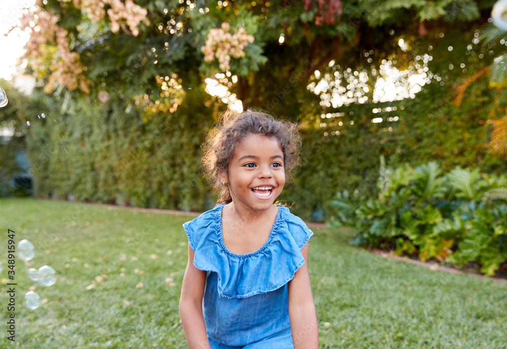 Young Hispanic Girl Chasing And Catching Bubbles In Garden Young Hispanic Girl Chasing And Catching Bubbles In Garden
