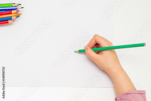 Top view of kid's hand drawing on the white paper with pencils. Concept of school activities. Copy space for text. Mock up.