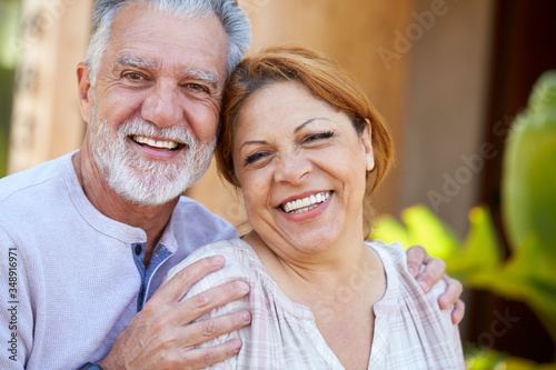 Portrait Of Smiling Senior Hispanic Couple Relaxing In Garden At Home Together