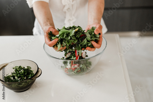 Young woman prepares lunch in cooking concept for kitchen, culinary, healthy lifestyle,vegetarian salad for a healthy diet,girl breaks greens and throws in a plate with salad