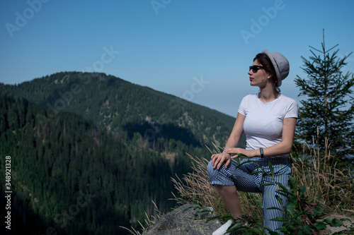 happy traveler hipster girl with windy hair in glasses, standing on top of sunny mountains. space for text. stylish woman in hat. atmospheric moment. travel and wanderlust. space for text