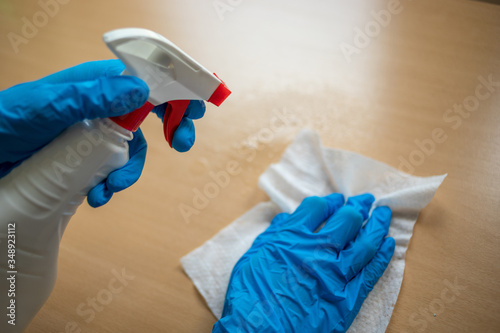 Cleaning home table sanitizing office table surface with disinfectant spray bottle washing surfaces with towel and gloves. COVID-19 prevention sanitizing inside. photo