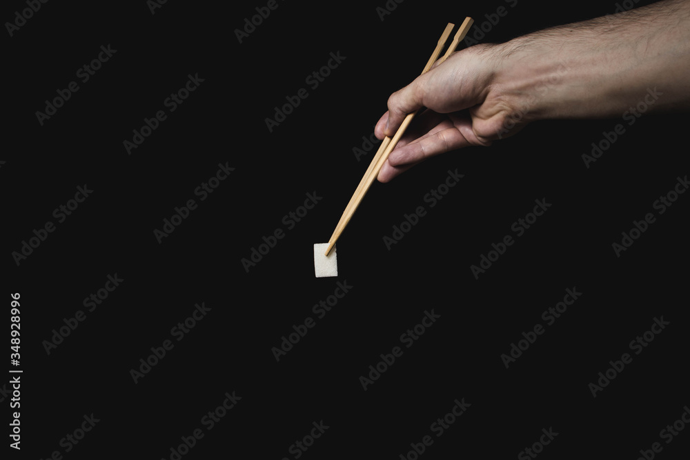 Hand holds sugar cube with Chinese chopsticks on black background Hand holds sugar cube with Chinese chopsticks on black background