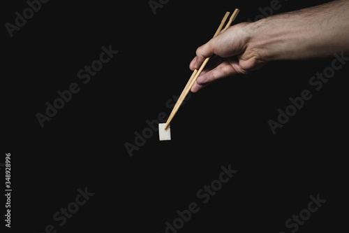 Hand holds sugar cube with Chinese chopsticks on black background