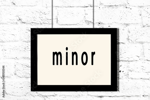 Black frame hanging on white brick wall with inscription minor