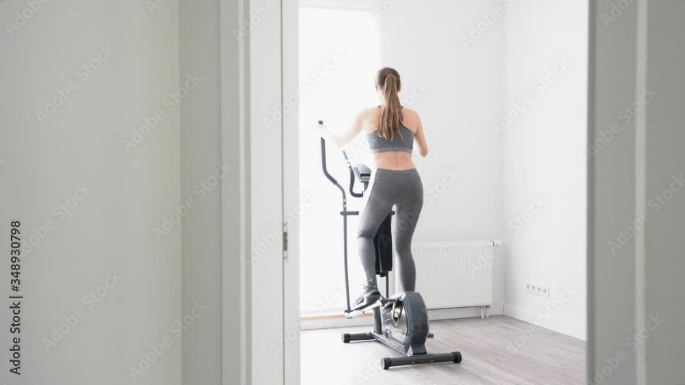 Rear view of young woman on cross trainer at home Rear view of young woman on cross trainer at home