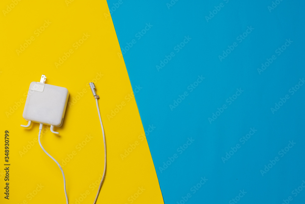 Laptop charger over blue yellow background. Battery life concept. topic of electric energy in travel. mobility concept. digital nomad concept. job online concept. copy space Laptop charger over blue yellow background. Battery life concept. topic of electric energy in travel. mobility concept. digital nomad concept. job online concept. copy space