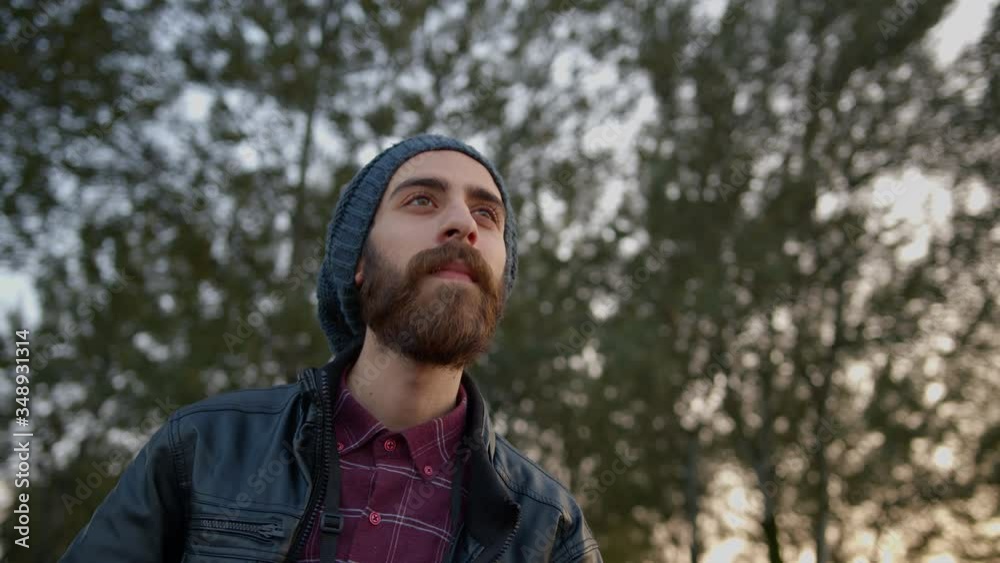 Hooded bearded young man with leather jacket is sees something far and uses the binoculars to see it. in the woods. slow motion Hooded bearded young man with leather jacket is sees something far and uses the binoculars to see it. in the woods. slow motion