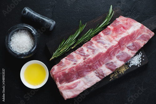 Raw fresh pork ribs with seasonings on a wooden cutting board, flatlay on a black stone background, horizontal shot