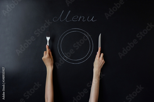 Knife and fork in hand near the drawn empty plate. Menu lettering on a black chalkboard