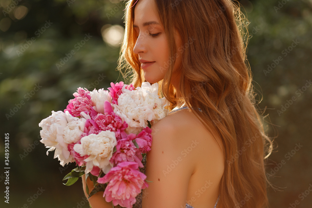 Fototapeta premium girl in the sun. Close-up portrait of a model with flowers in the summer. walk in the park in spring. cosmetics and beautician. blurred background, art effect. peonies. summer flowers
