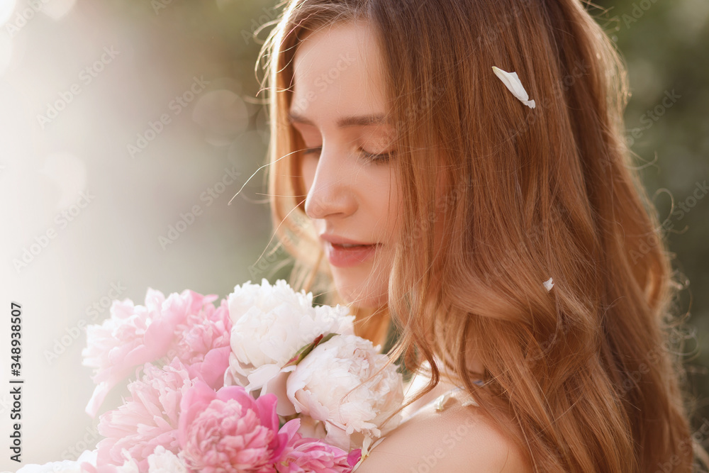 Naklejka premium Close-up portrait of a model with flowers in the summer at sunset. girl with peonies. blurred background, concept