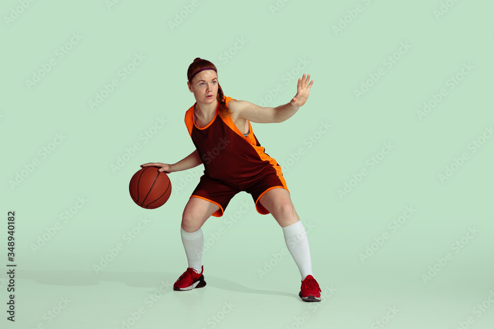 Young caucasian female basketball player in action, motion during gameplay isolated on mint colored background. Concept of sport, movement, energy and dynamic, healthy lifestyle. Training, practicing.