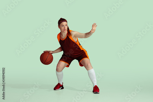 Young caucasian female basketball player in action, motion during gameplay isolated on mint colored background. Concept of sport, movement, energy and dynamic, healthy lifestyle. Training, practicing. © master1305