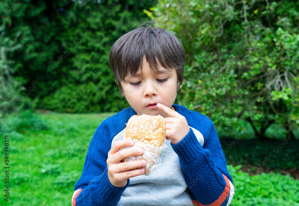 Hungry boy eating homemade bread sandwiches with mixed vegetables in the park, Child siting on green grass eating his snack picnic with blurry trees background, Spring outdoor activity Hungry boy eating homemade bread sandwiches with mixed vegetables in the park, Child siting on green grass eating his snack picnic with blurry trees background, Spring outdoor activity