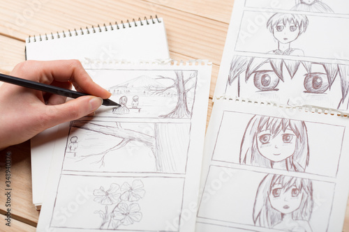 Artist drawing an anime comic book in a studio. Wooden desk, natural light. Creativity and inspiration concept. photo