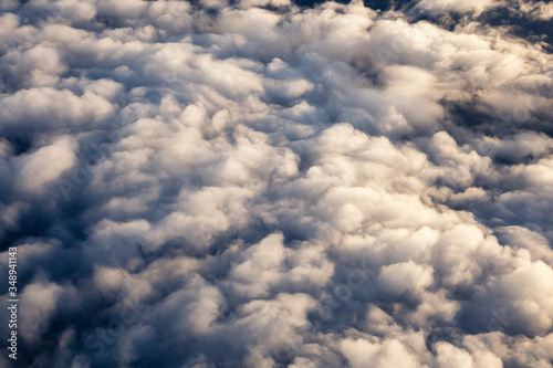 Aerial view from above a white and puffy clouds during a sunny sunrise. Taken from Airplane in British Columbia, Canada.