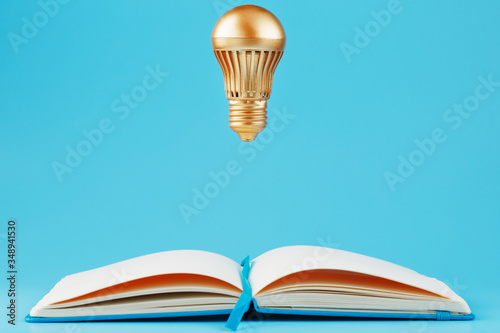 A gold-colored light bulb hangs above the blank pages of a notebook on a blue background.