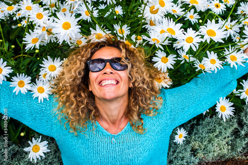 Joyful and mindulness concept with cheerful young caucasian woman lay down in a natural flowers background on the ground - spring and summer season and outdoor active leisure activity for happy people photo