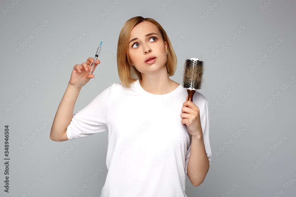Close up woman holding syringe with mesotherapy injection and hairbrush in hand, choosing hair loss problem care product. Cosmetology and beauty industry. Benefits and side effects of procedure