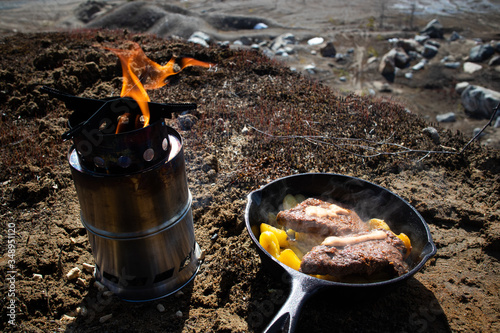 Cooking steaks and potatoes with cast iron frying pan next to sand pit at spring time.
