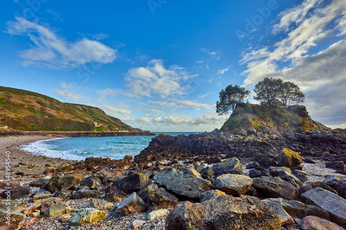 Image of Bouley Bay with beacha and harbour with stones in the foreground. Jersey Channel Islands