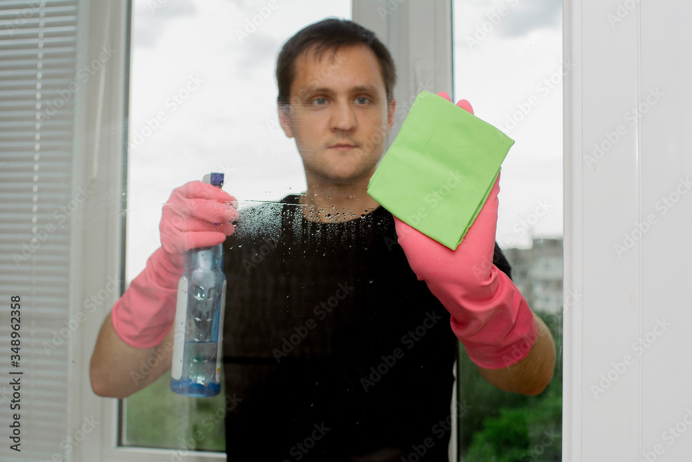 young guy in pink rubber gloves holds window cleaner and rag and washes plastic windows young guy in pink rubber gloves holds window cleaner and rag and washes plastic windows