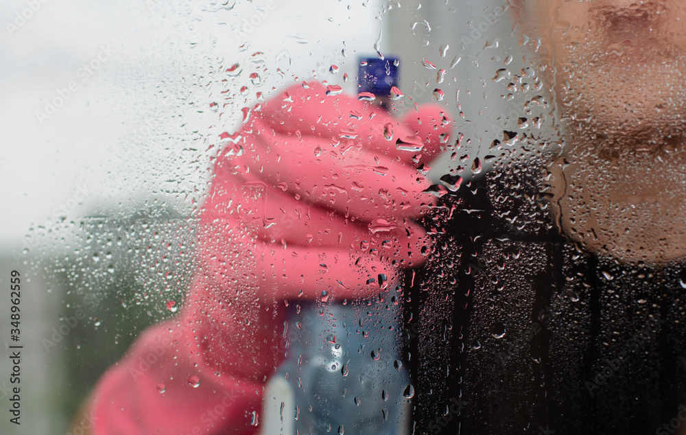 Fototapeta premium young guy in pink rubber gloves holds window cleaner and rag and washes plastic windows